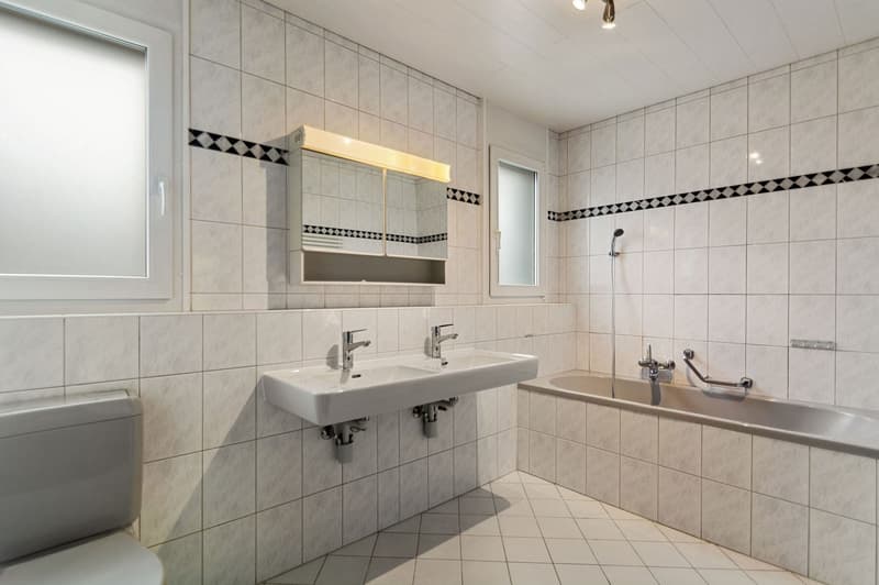 White tiles, double sink, toilet, bathtub, shower head, mirror
