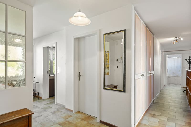 Corridor with wooden floors, modern mirror, and two doors; features a ceiling lamp and tiled floor