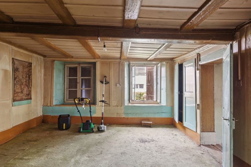 empty room, wooden ceiling, two windows, two doors, two lawn mowers, small stool, painting on wall