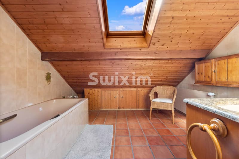Salle de bain sous combles avec baignoire, plafond en bois, et puits de lumière.
