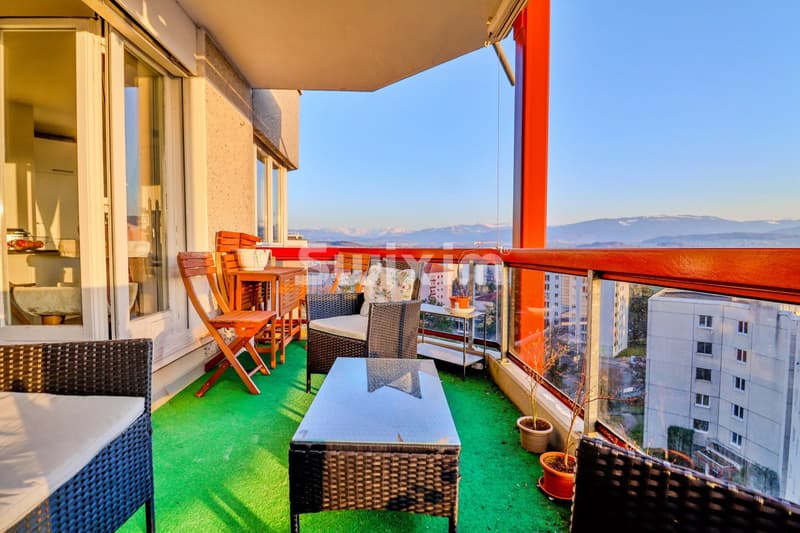 Balcon aménagé avec des meubles en rotin, vue sur la ville et les montagnes au loin.