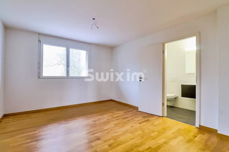 Suite parentale avec parquet, une fenêtre, et une porte ouverte vers une salle de bain.