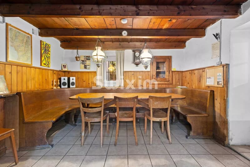 Une salle à manger en bois rustique avec des chaises autour d'une grande table, éclairée par deux suspensions.