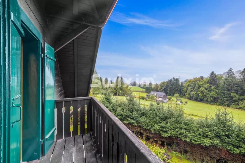 Balcon en bois avec vue sur la campagne et les arbres verdoyants.