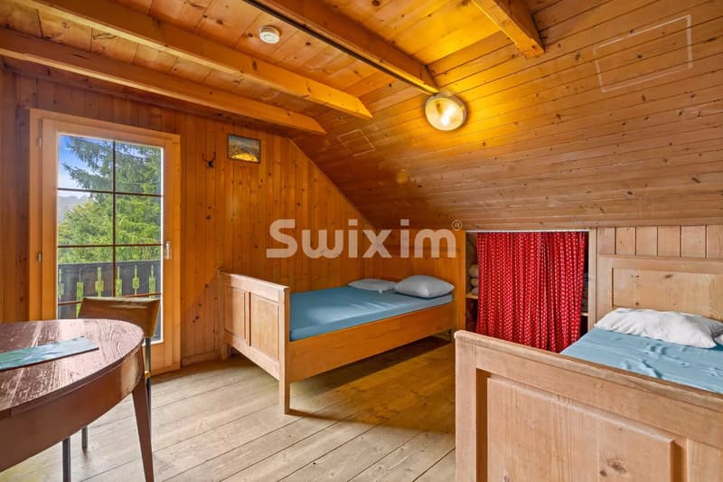 Une chambre en bois chaleureux avec deux lits simples, une fenêtre donnant sur des arbres et un rideau rouge.