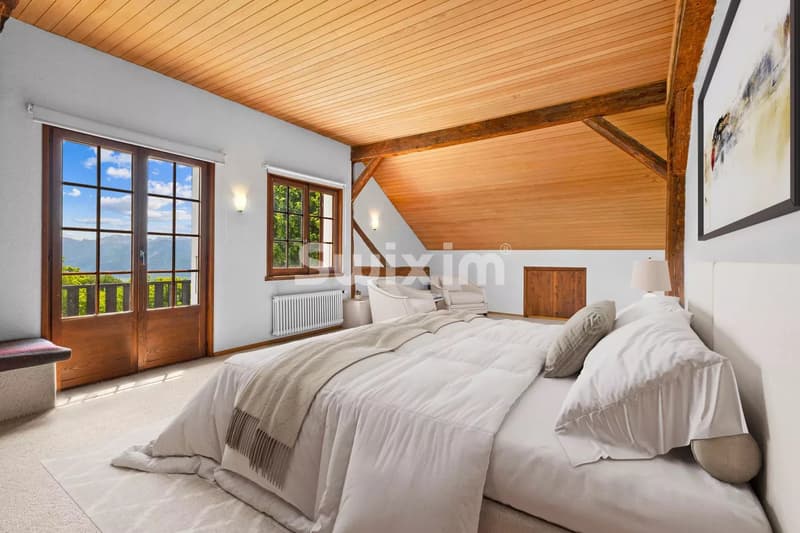 Chambre lumineuse avec un grand lit, plafond en bois et vue sur la nature par la fenêtre.