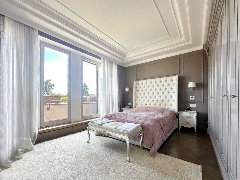 Tufted headboard, white bed, pink blanket, large windows, white curtains, white bench, wood floor, beige rug, wall lamps, nightstands, white built-in wardrobes