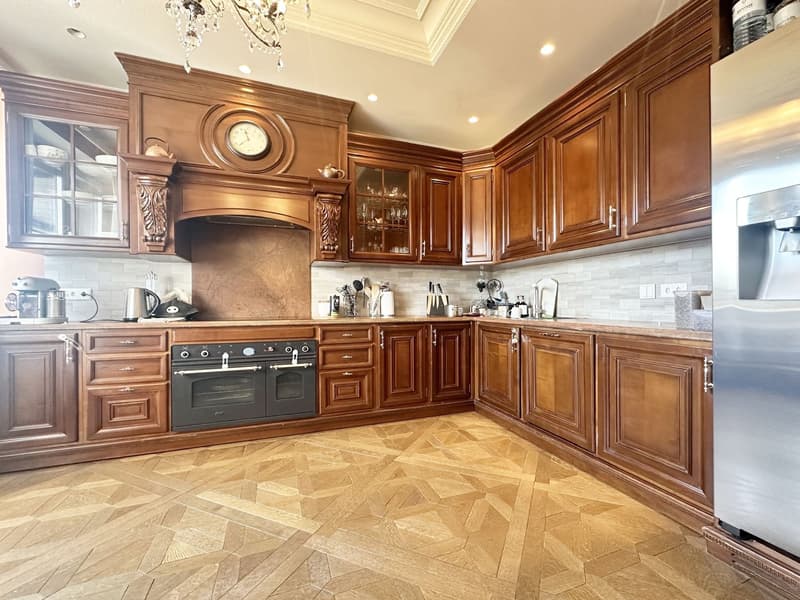 wooden cabinets, wooden floor, chandelier, clock, stove, refrigerator, countertop, sink, faucet, knives