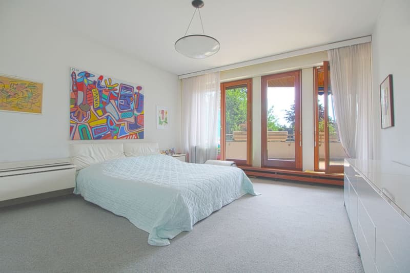 A large bed with white cover, a cabinet, and two pictures. It has a glass door that leads to a balcony