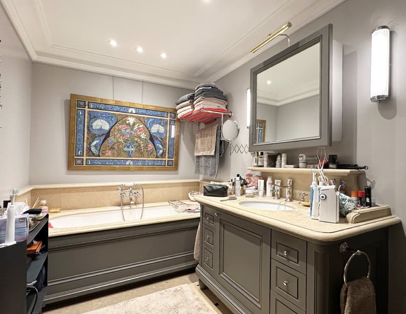 Bathroom with beige bathtub, gray cabinets, countertop, mirror, sink, towels rack, artwork