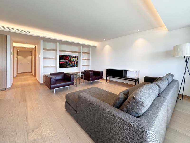 modern living room with gray sofa, brown armchairs, TV, wooden floor, white walls, shelves, table, lamp
