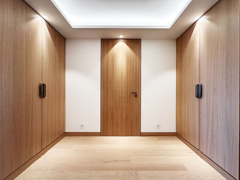 Empty room with wooden cabinets, wooden door, wooden floor, white walls, ceiling lights