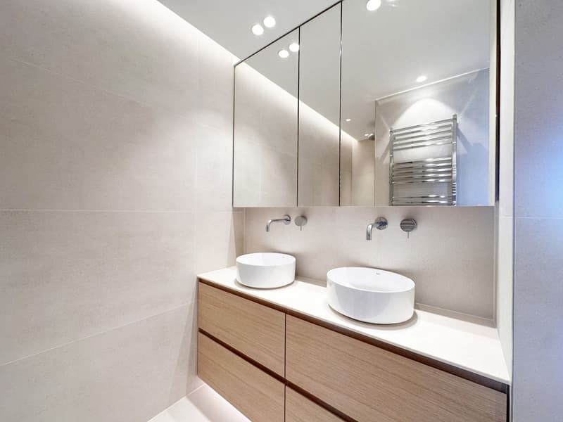 modern bathroom with two sinks, wooden cabinets, large mirror, and a towel rack