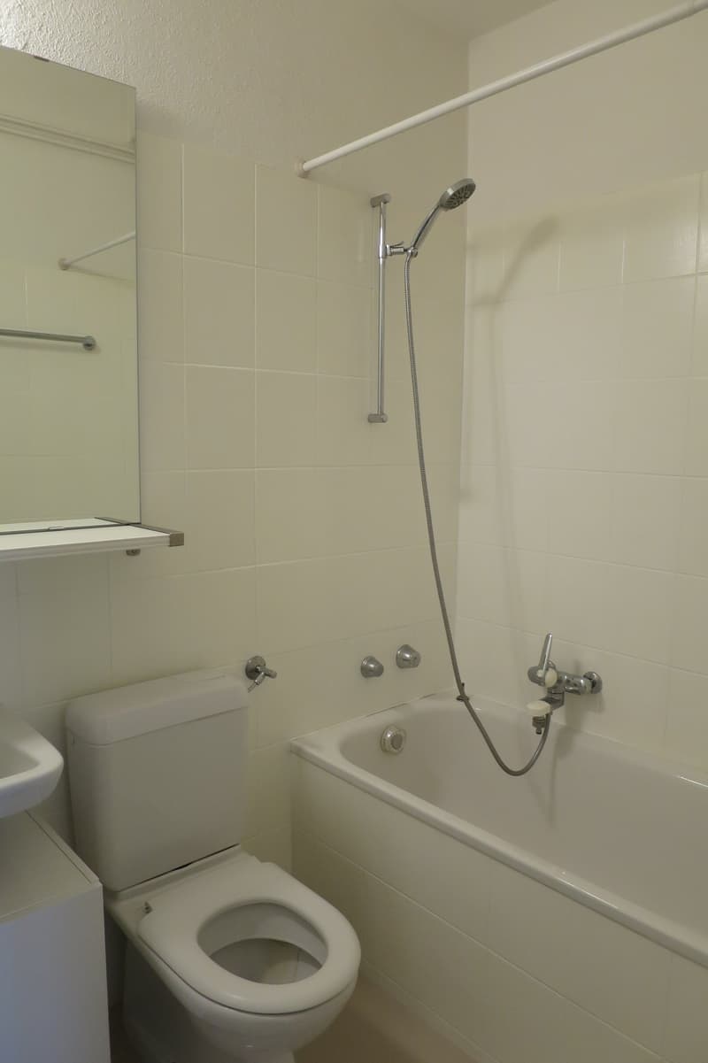 Bathroom with a white bathtub, toilet, sink, and shower head attached to the wall.