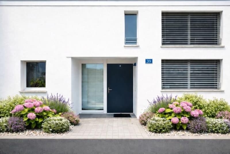 White building, 3rd floor, gray tiled entrance, black door, flowers in front, multiple windows