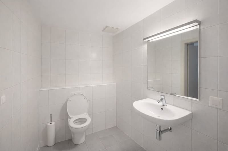 modern bathroom with white tiles, toilet, sink, mirror, wall-mounted towel holder, illuminated mirror, toilet paper holder