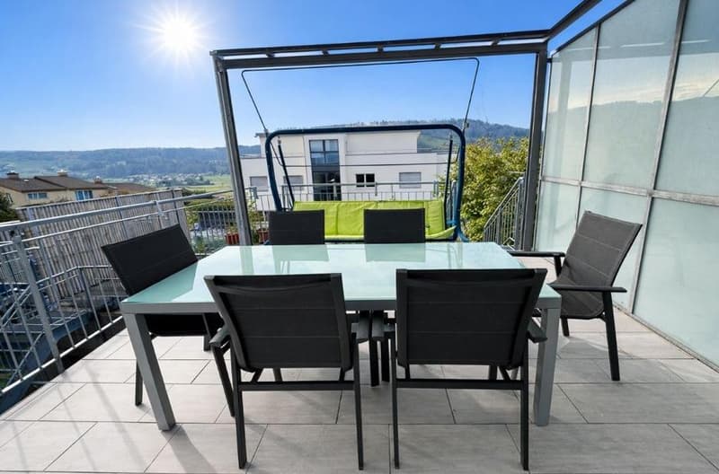 Balcony with dining table, chairs, glass railings, garden swing, glass enclosures, scenic view