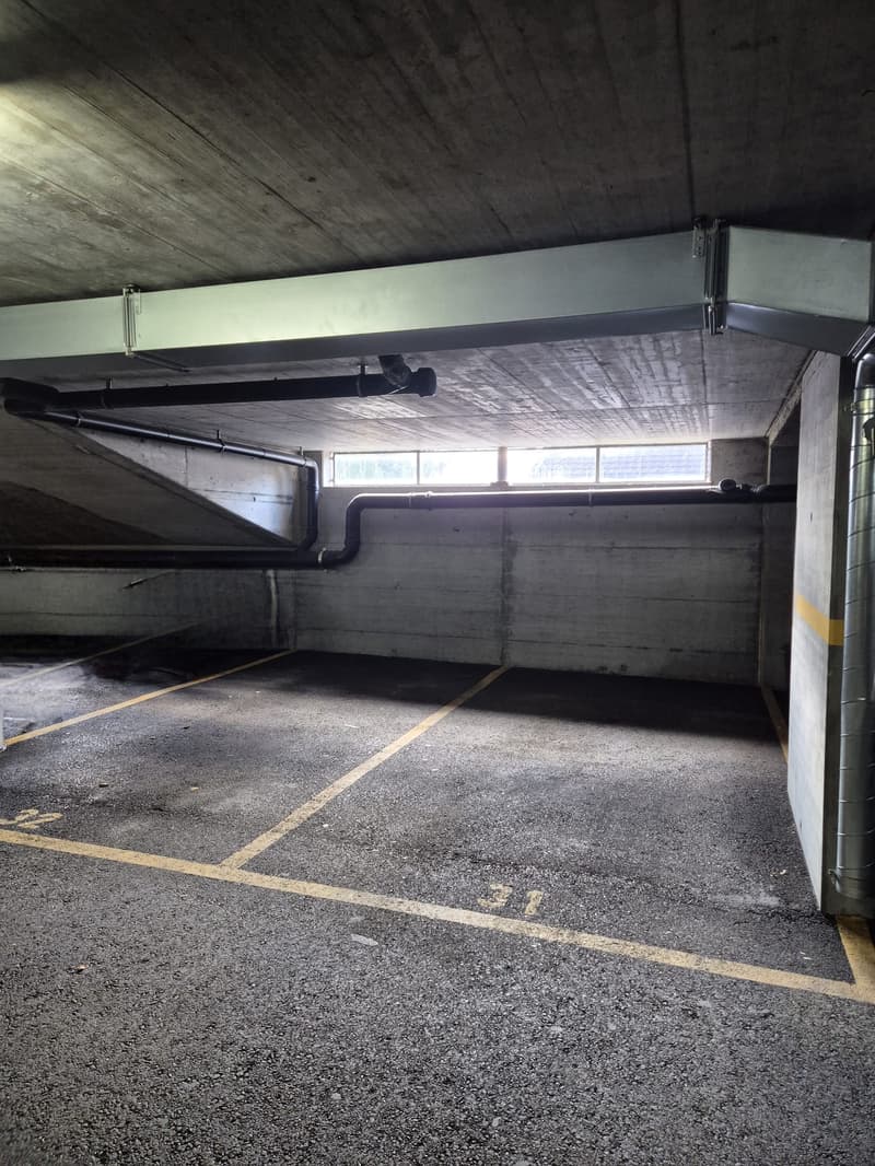 Parking lot, concrete ceiling, yellow markings on the floor, pipes along the ceiling