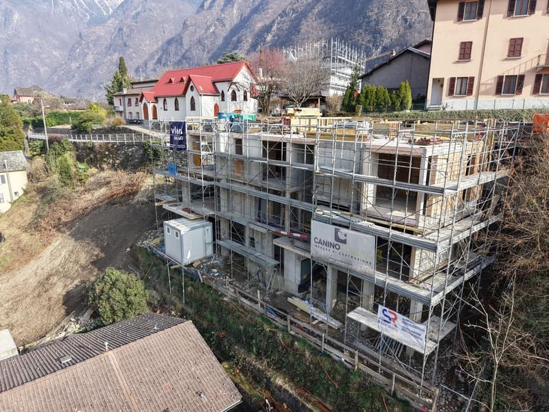 Building under construction, scaffolding, multiple floors, red roof, surrounded by other buildings and mountains