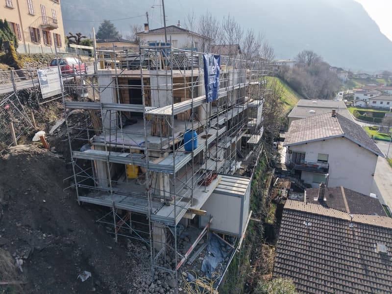 Aerial view of a multi-story house under construction with scaffolding, located on a slope with a mountain in the background.