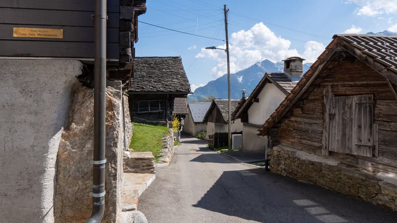 Wooden houses, stone walls, narrow street, mountains in the background