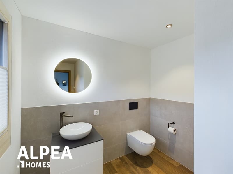 circular mirror, white toilet, white sink, white cabinets, tiled walls, hardwood floor