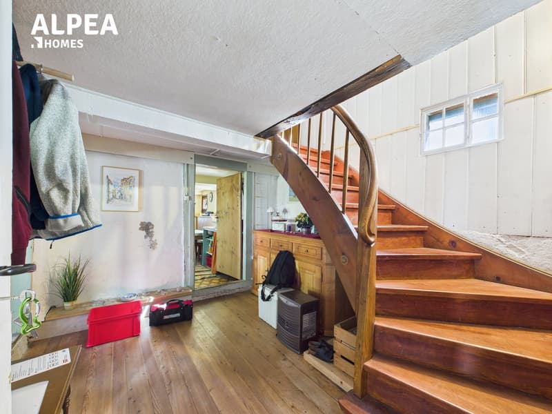 Entrance with wooden stairs, wooden floor, wooden cupboard, small potted plant, picture frame on the wall, jacket on the hanger, red storage box on the floor