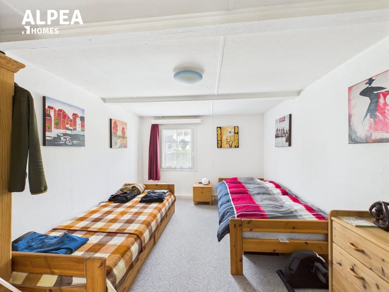 two wooden single beds, bedside tables, window with red curtains, paintings on the wall, closet