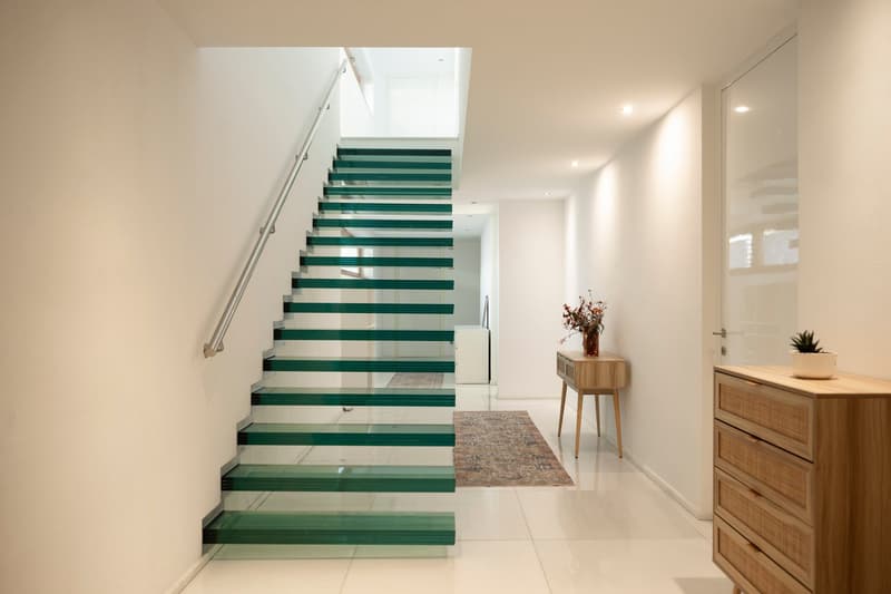 Modern house with glass staircase, white walls, white tiles, wooden cabinet, flower vase, rug