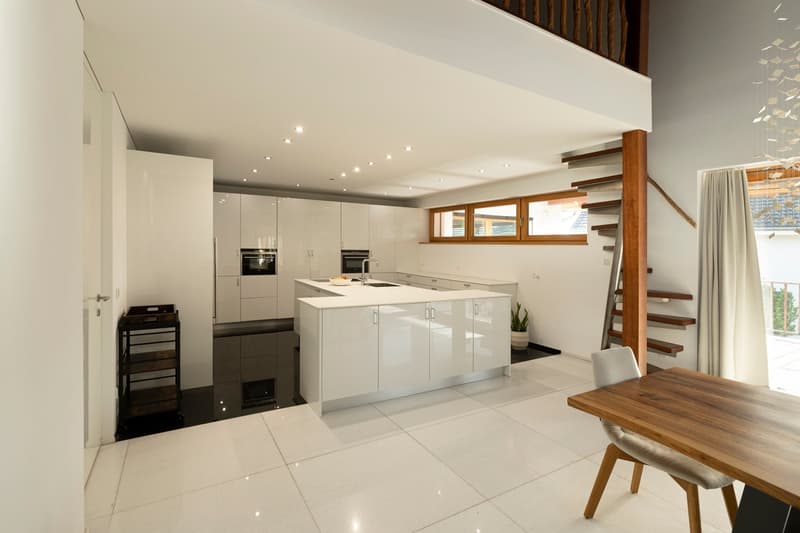 modern kitchen with white cabinets, island, black floor, dining area with wooden table, staircase, balcony