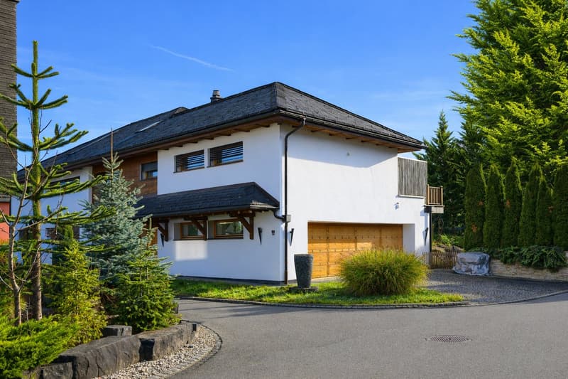 2 story house, white exterior, black roof, wooden garage, large windows, surrounded by trees
