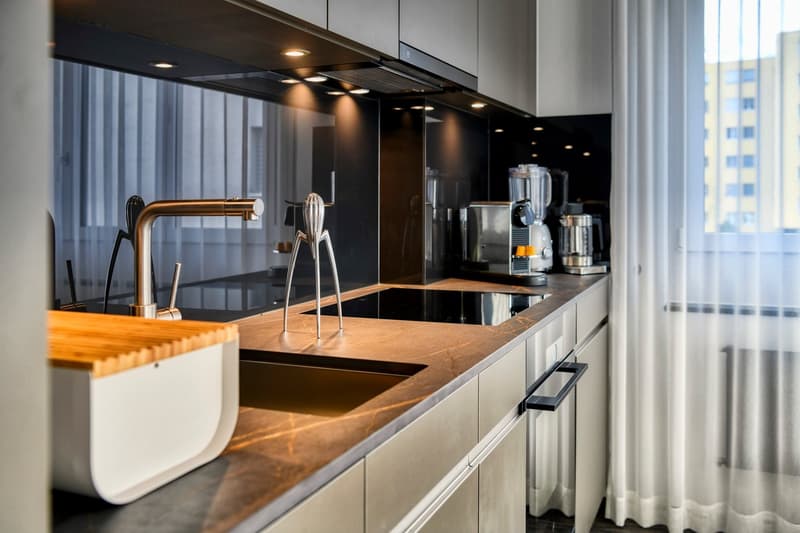 Modern kitchen with black cabinets, wooden countertops, stainless steel appliances including a dishwasher, and a large window providing natural light