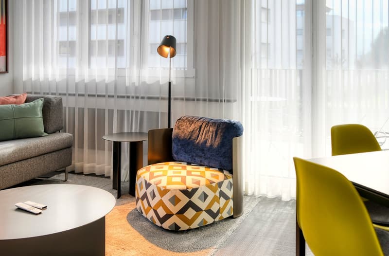 Large windows, gray sofa, patterned ottoman, yellow chairs, side table, floor lamp