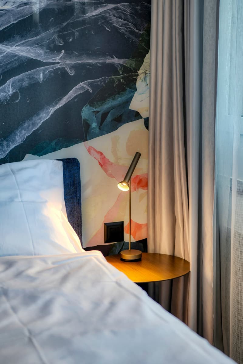 Bedroom with large window, floral wallpaper, bedside table with lamp, and curtains