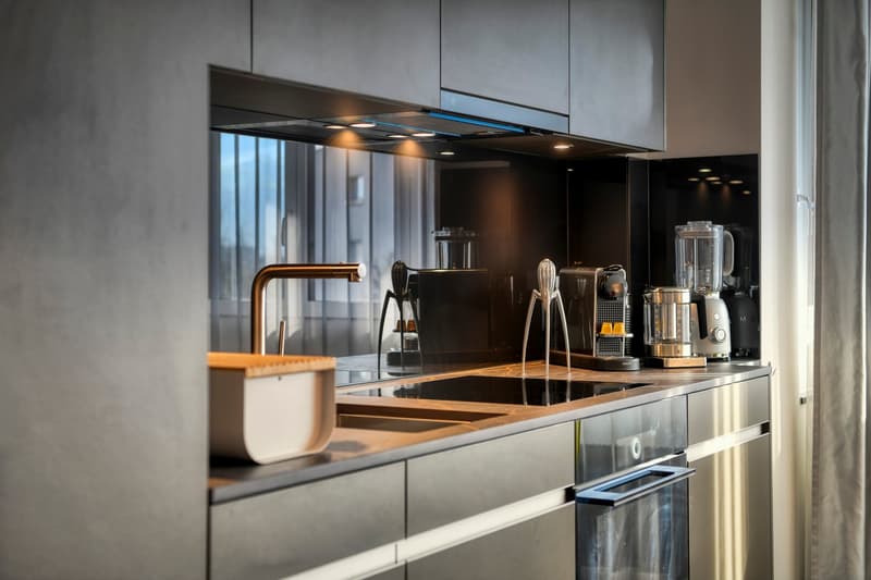 Modern kitchen with sleek black cabinets, copper faucet, kitchen appliances such as a blender and coffee maker, and a glass cooktop with a range hood above.