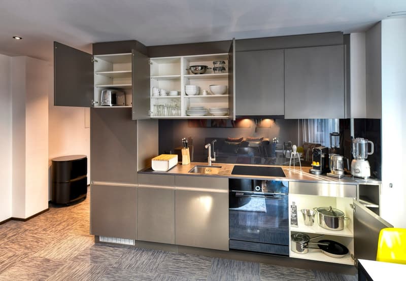 Modern kitchen with gray cabinets, wooden countertops, built-in appliances including a dishwasher, and open shelving displaying dishes and cookware.