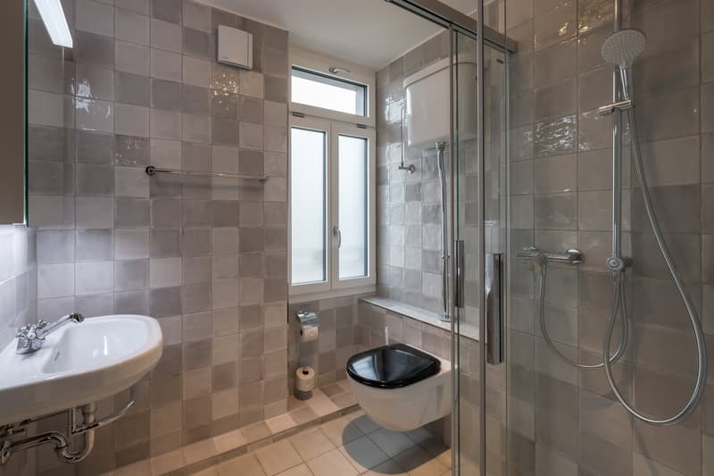 Tiled bathroom with a shower enclosure, toilet, sink, and a window providing natural light.