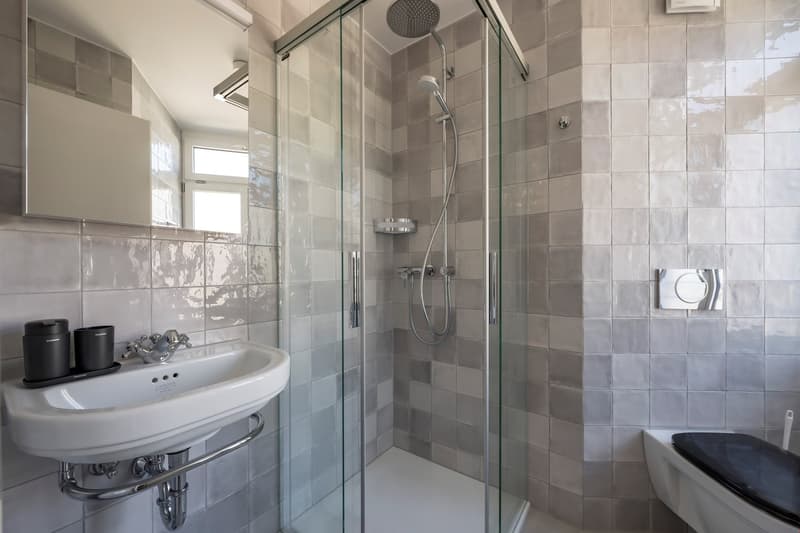 Modern bathroom with shower enclosure, white sink, mirror, and tiled walls.