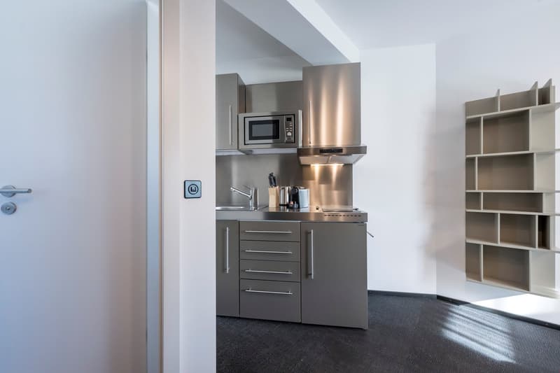 Compact kitchenette with stainless steel appliances, including a microwave and dishwasher, built-in cabinets, and a sink with a faucet.