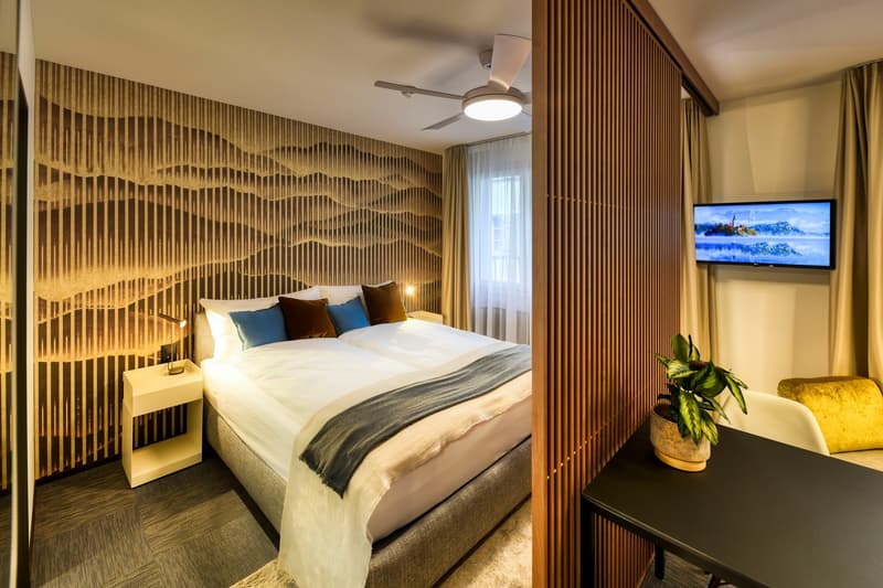 Spacious bedroom with wooden slat wall feature, large bed with bedding, side tables, flat-screen TV, and a potted plant