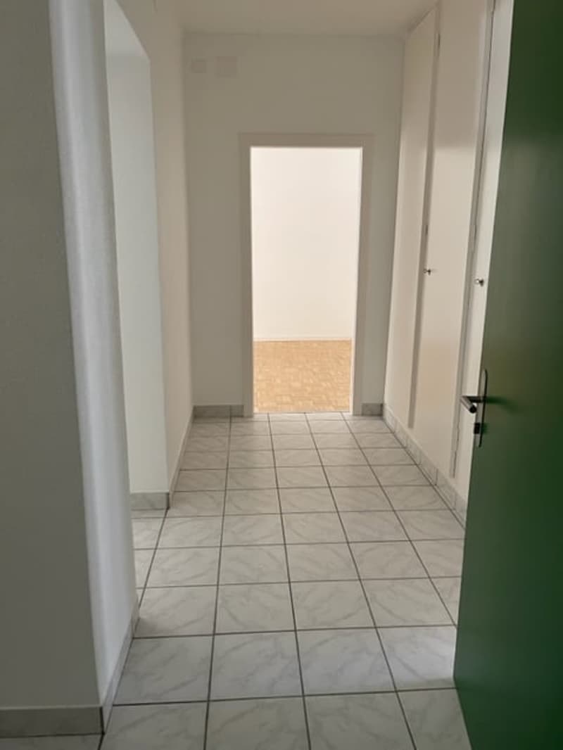 empty hallway with tiled floor, white walls, open doorway, and another room at the end