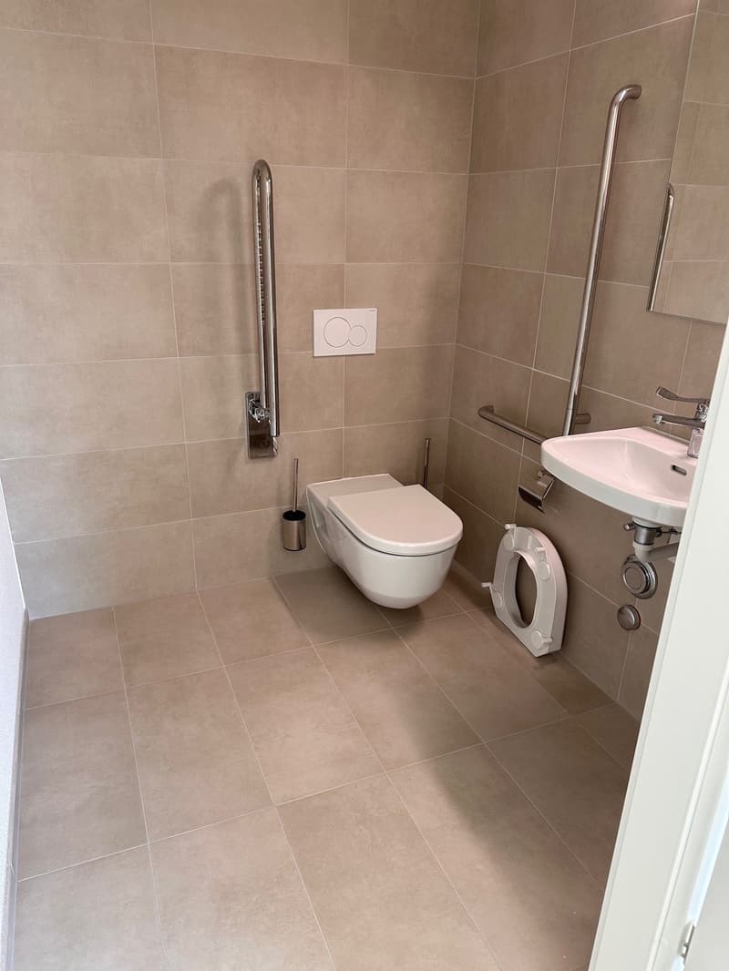 Accessible bathroom with tiled floor, white walls, toilet, sink, and grab bars