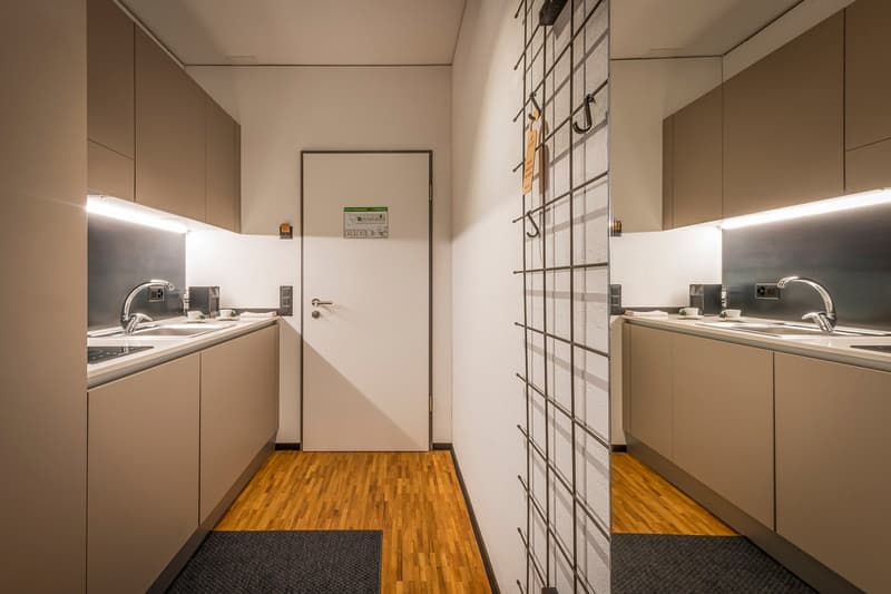 Compact laundry room with built-in cabinets, washing machine, and dishwasher. Hardwood flooring and a large window provide natural lighting. The room has a minimalist and modern design.