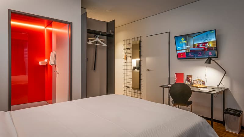 Modern bedroom with red accent wall, wardrobe, desk, TV, and amenities like dishwasher
