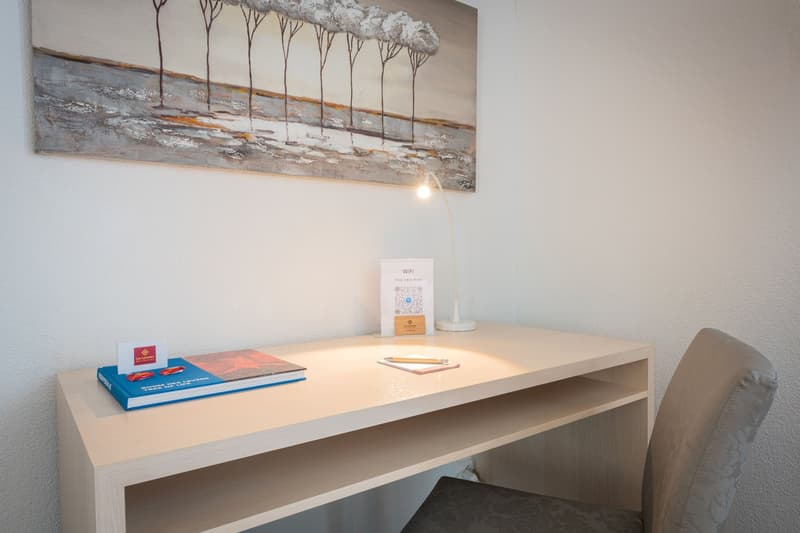 Desk with books, laptop, and WiFi sign, wall art depicting a snowy landscape, lamp, and comfortable chair