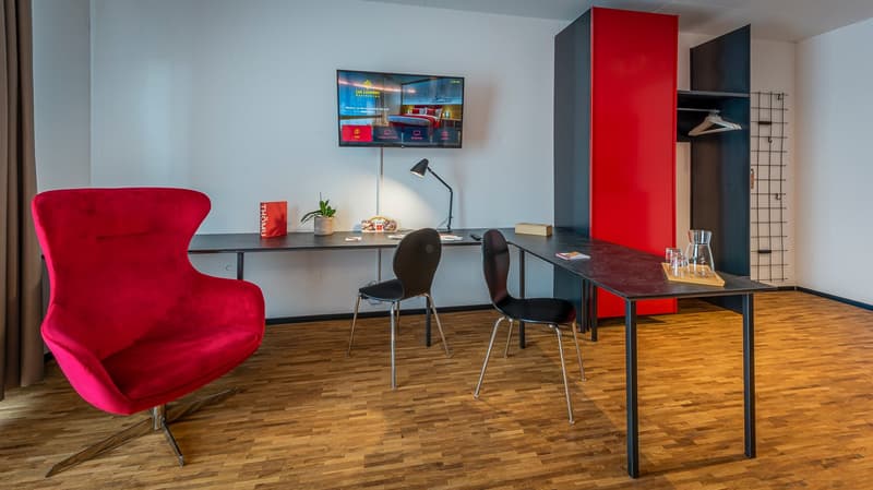 modern room with wooden floor, desk, red chair, black chairs, lamp, TV, plant, storage cabinet, curtain