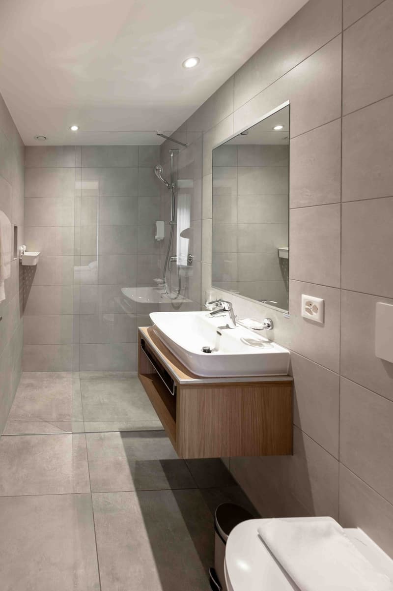 modern bathroom with shower, sink, toilet, mirror, and tiled flooring
