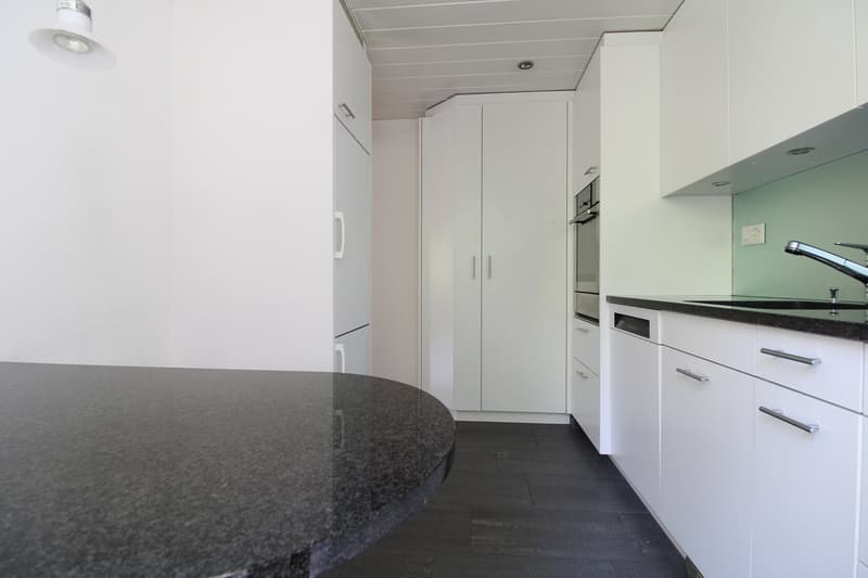 Modern kitchen with granite countertop, black flooring, white cabinets, integrated dishwasher, wall-mounted oven, sink with faucet, and a power outlet