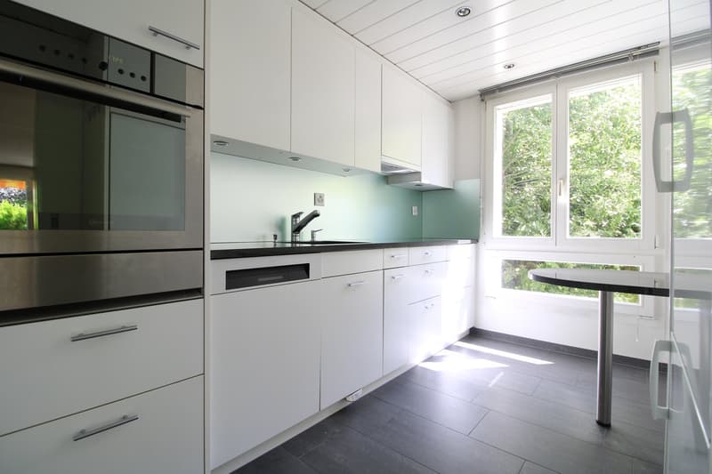 modern kitchen with white cabinets, black countertops, integrated dishwasher and washing machine, faucet, glass table