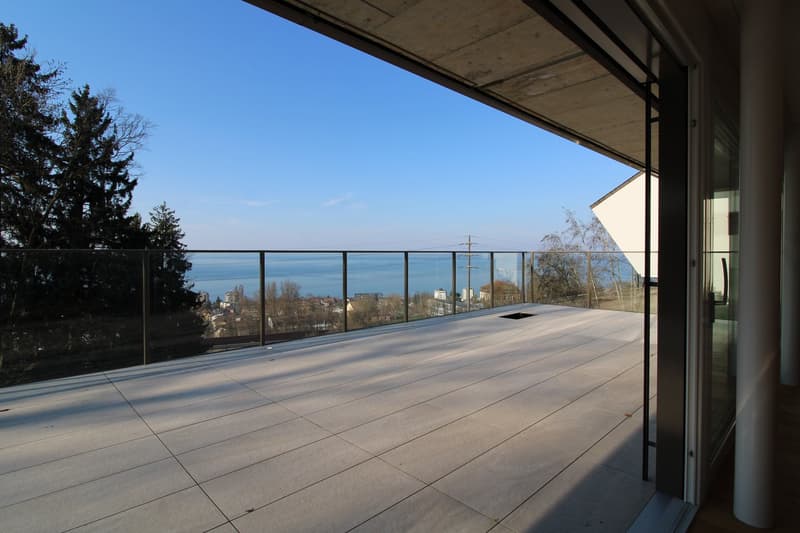 large balcony with glass railing, wooden floor, view of the sea and city